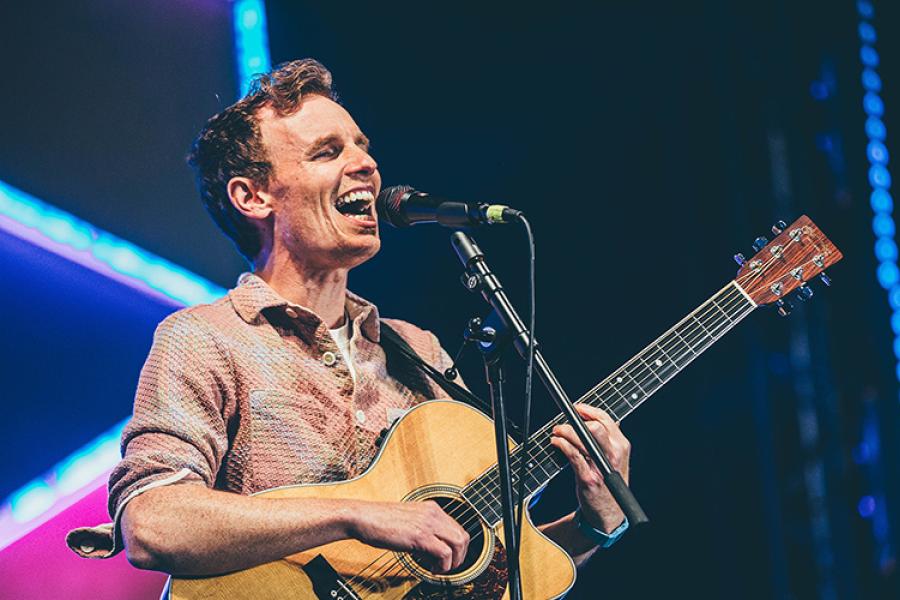 Person singing into a microphone and playing the guitar