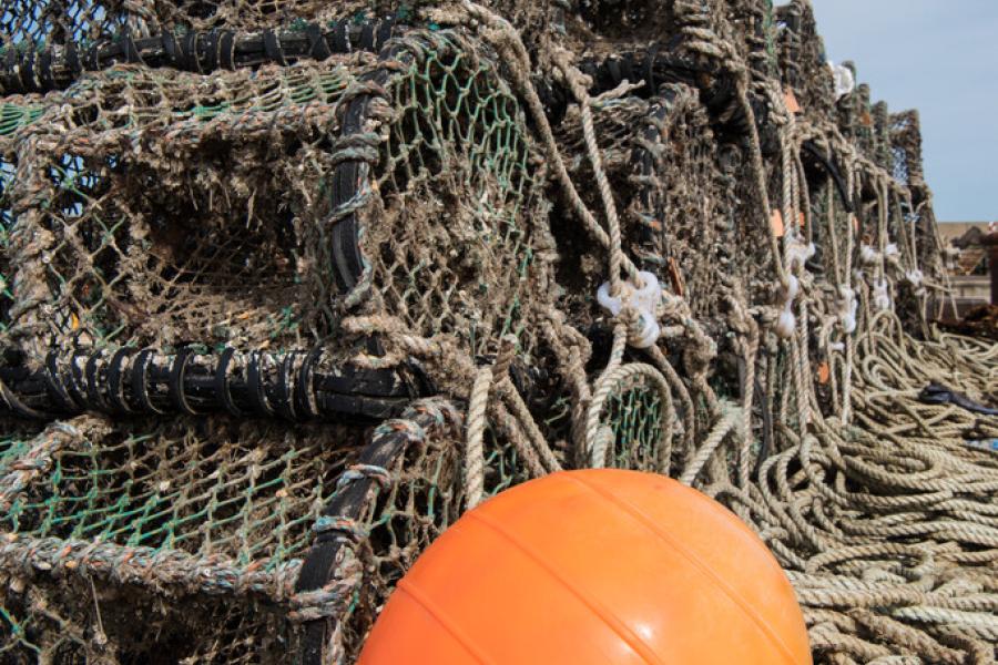 stack of lobster pots on the shore with an orange buoy