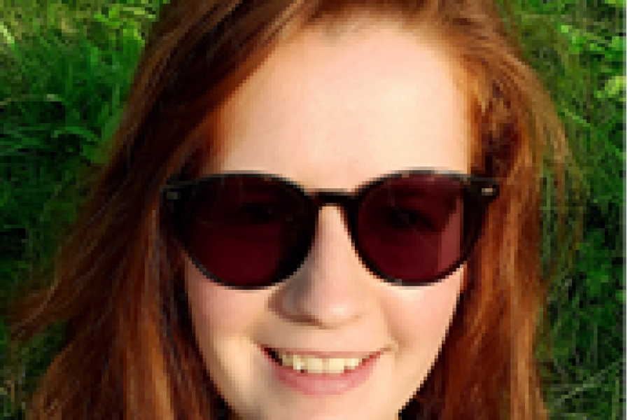A woman with ginger hair wearing sunglasses lies on the grass smiling.