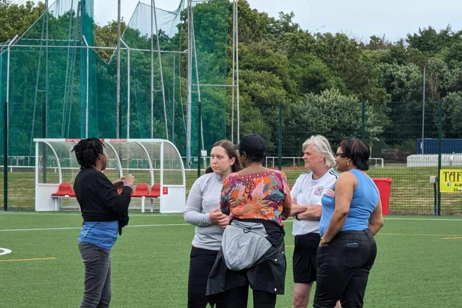 a group of displaced citizens congregating on a football pitch enjoying a chat with members of a local charity football team 