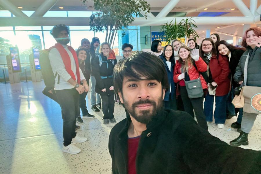 A student taking a selfie with a group of students in the background in an airport