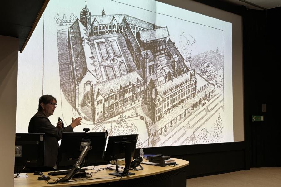 Gari Wyn in front of big screen showing original plans of the University