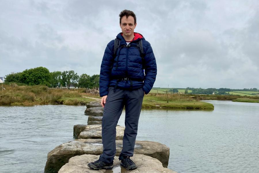 A photograph of Dr Richard Dallison standing on large rock stepping stones in the middle of a wide river.