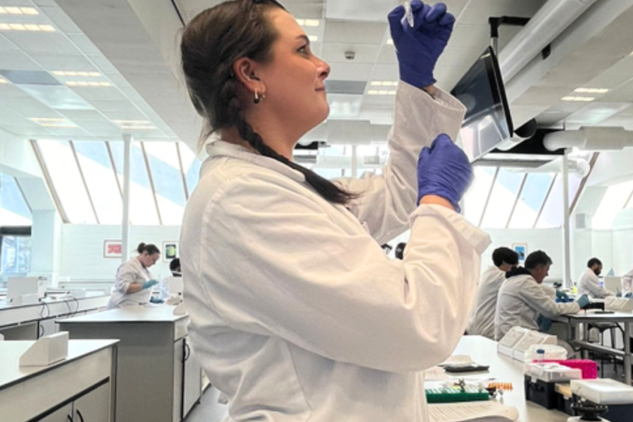 a female university student in a lab is wearing blue gloves, holding up a vial