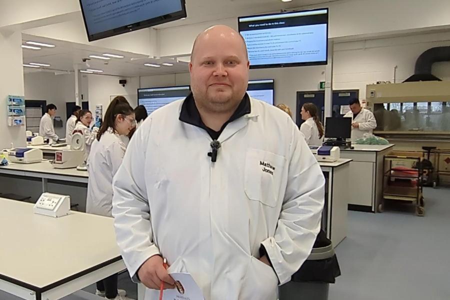 Mathew Jones, a male lecturer stands in  the foreground of a laboratory where students are doing practical work in the background