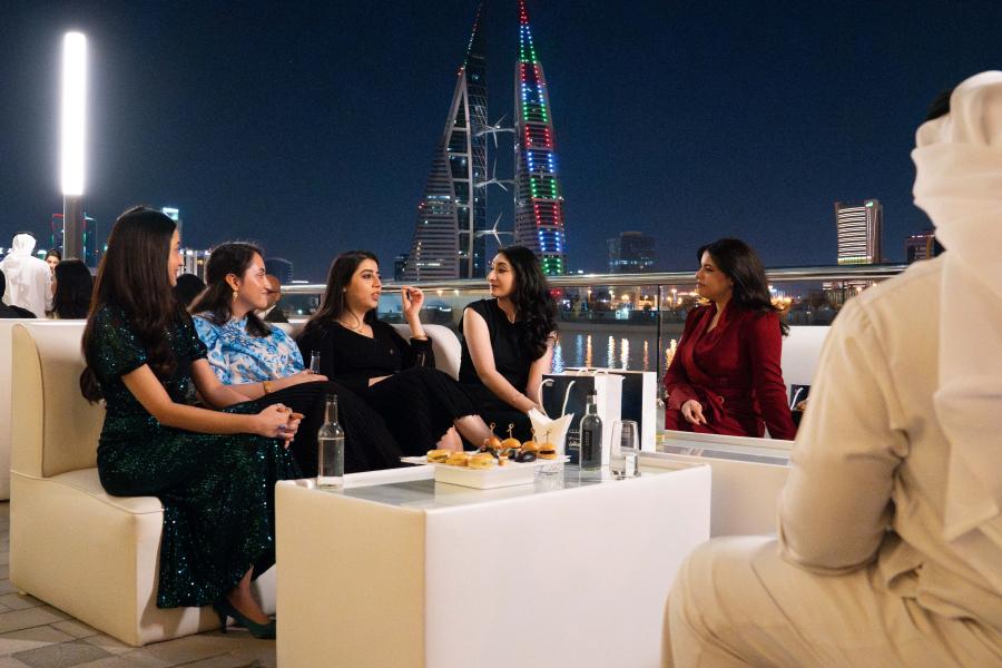 Five alumni sitting and chatting in front of Bahrain skyline