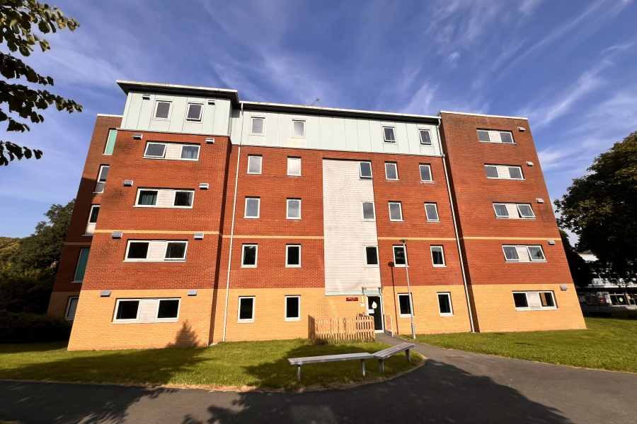 Ffraw Hall - 5 story building cladded in brick. First floor in yellow, middle two in light brown and top in green. Sunlit in a green surrounding. 