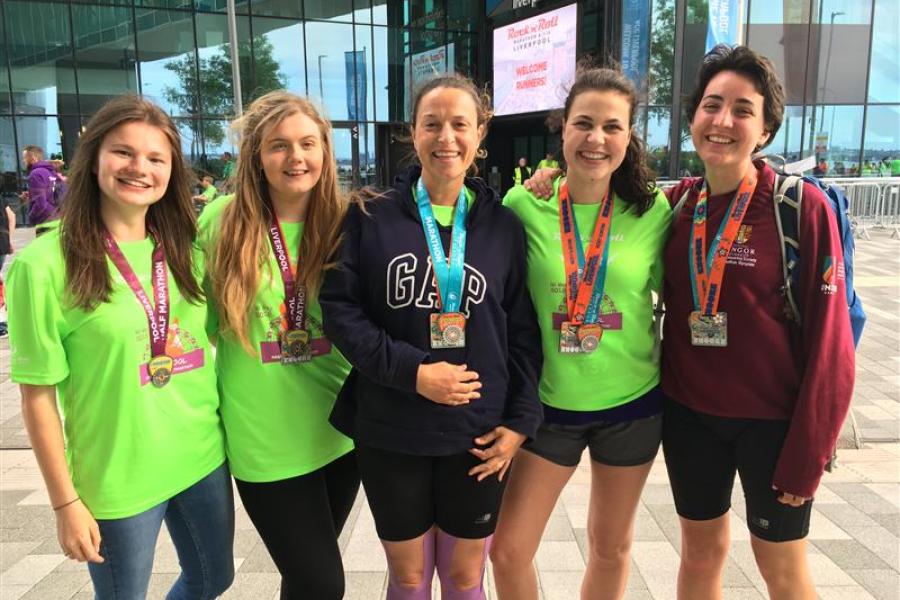 Dr Fran Garrad-Cole in the middle and four students from the Born to Run module in running gear wearing medals after a marathon