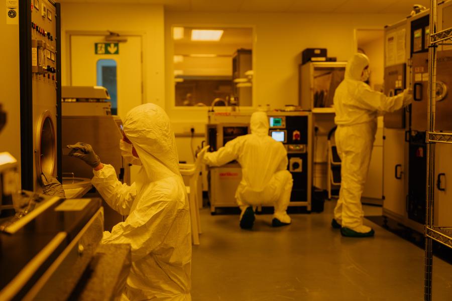 Three students dressed in white, clean-room coveralls, using the equipment in Bangor University's clean room.