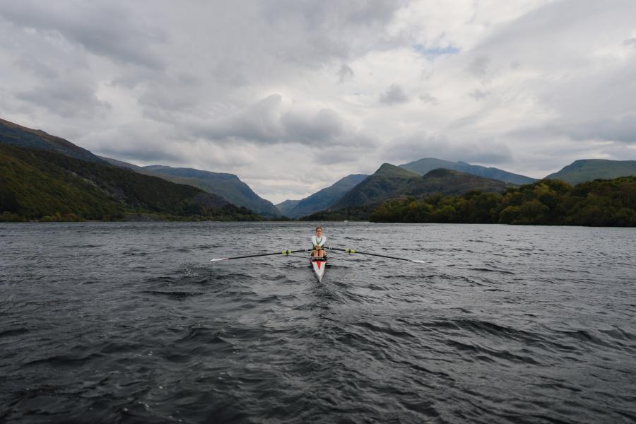 A student rows across Padarn Lake, framed by the moody, dramatic peaks of Eryri, including Yr Wyddfa (Snowdon), in the background.