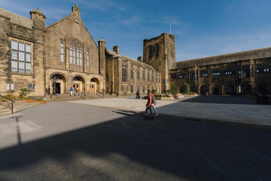 The beautifully lit Main Arts Building stands beyond the Outer Quad, as two students walk toward its entrance from the direction of the library.