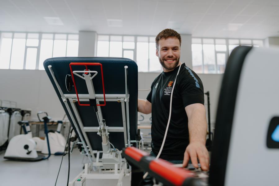 Academic in black Bangor Sport Science T-shirt doing lab work smiling at the computer