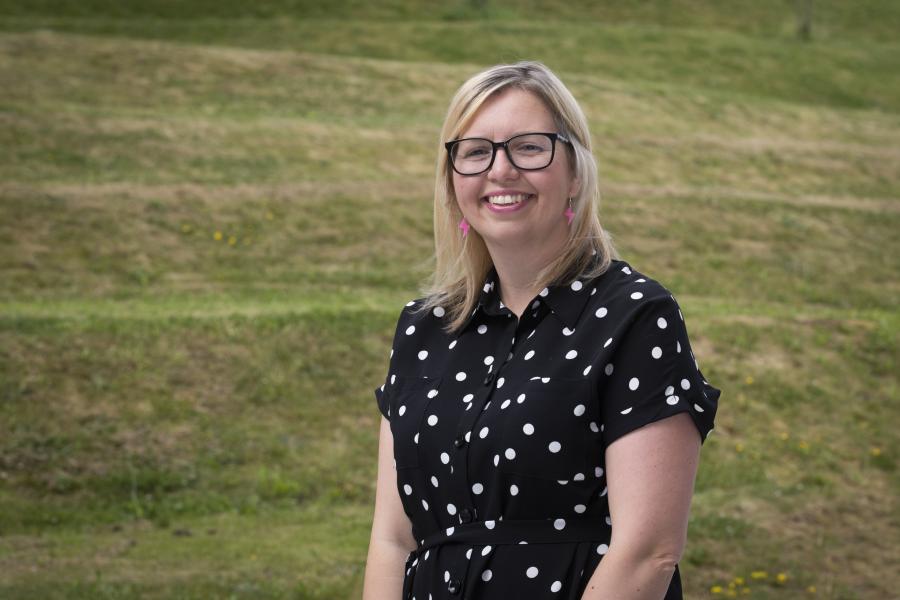 Spectacled woman with blond shoulder length hair sits in from of cut grass