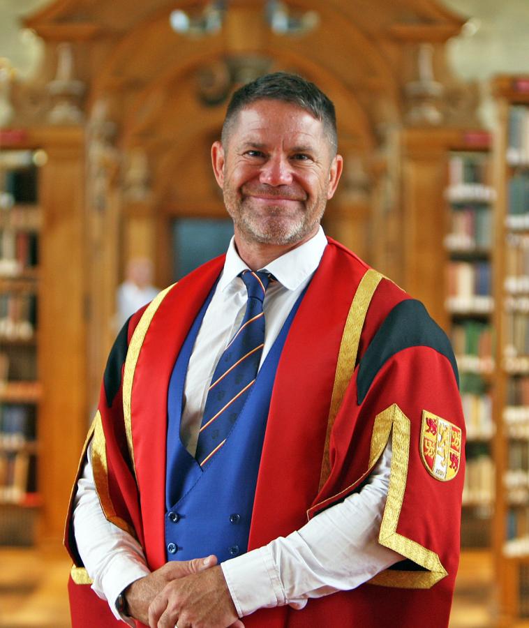 Photo of Mr Steve Backshall in Bangor University library in graduation gown