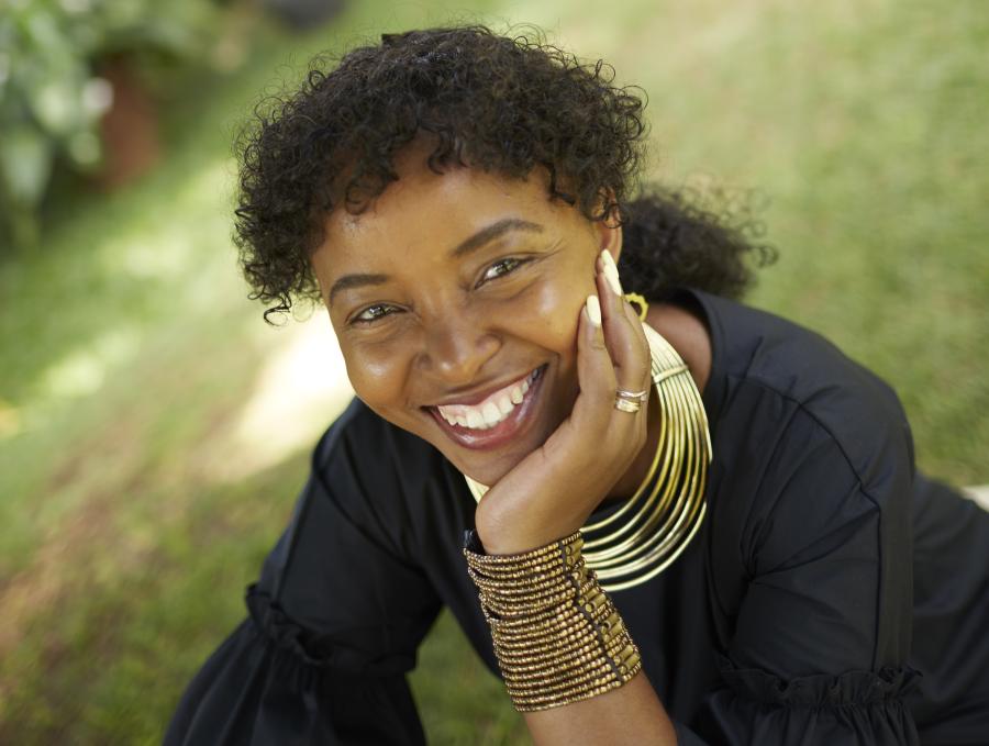 woman smiles up towards camera with face leaning on hand.