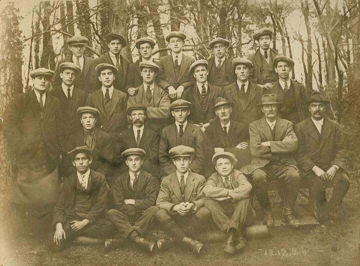 An old sepia photograph of a group of Penrhyn Estate workers wearing suits and caps. 