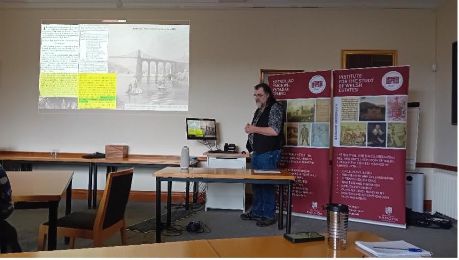 Doctoral researcher Peter Crosby standing in front of a presentation on a screen.