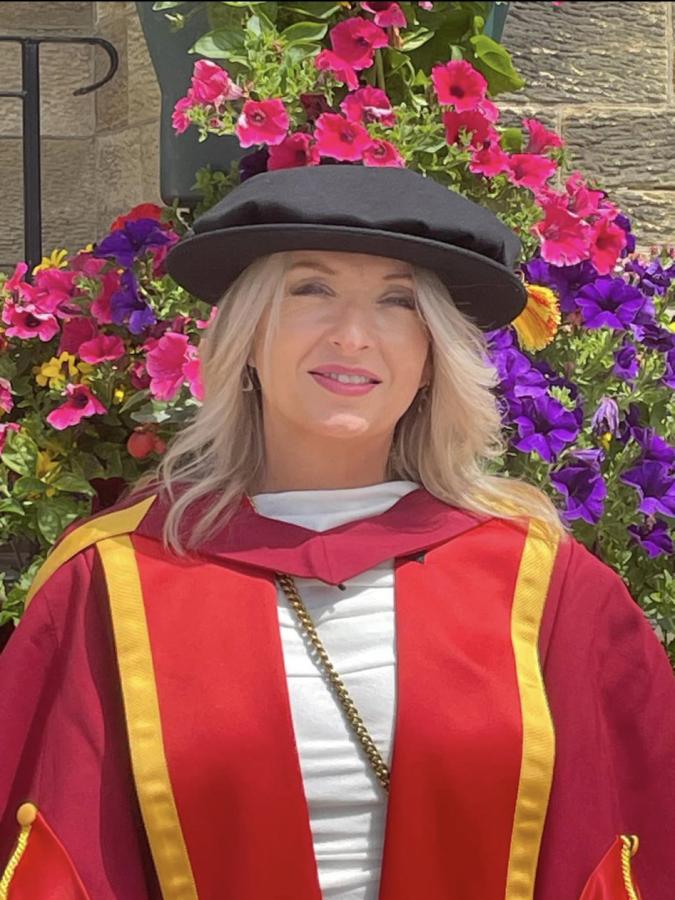 Doctoral researcher Meinir in a red and gold graduation gown