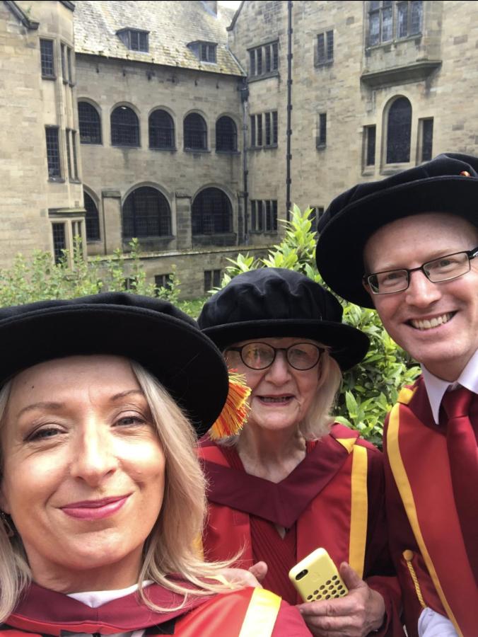 A "selfie" photograph of Meinir in her Doctoral robes on the grounds of Bangor University, with her fellow doctoral graduate, Dr Mary Oldham, and supervisor, Dr Shaun Evans