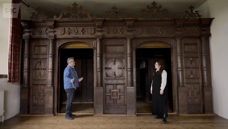 Presenters Aled and Bethan stand in front of the wooden, Mannerist screen in the Hall at Treowen.